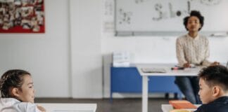 Od nieśmiałka do lidera – jak wspierać kompetencje społeczne w klasach 1–3 Dwójka uczniów rozmawia w klasie, w tle nauczyciel