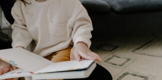Książki o ciele i granicach, które pomogą dziecku powiedzieć nie i zadbać o siebie Małe dziecko siedzi na dywanie i czyta kolorową książkę z obrazkami