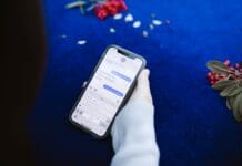 Aplikacja do kontaktu z rodzicami – jak wybrać bezpieczne i wygodne rozwiązanie? Osoba trzymająca smartfon z wiadomościami tekstowymi na niebieskim tle z kwiatam