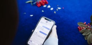 Osoba trzymająca smartfon z wiadomościami tekstowymi na niebieskim tle z kwiatam