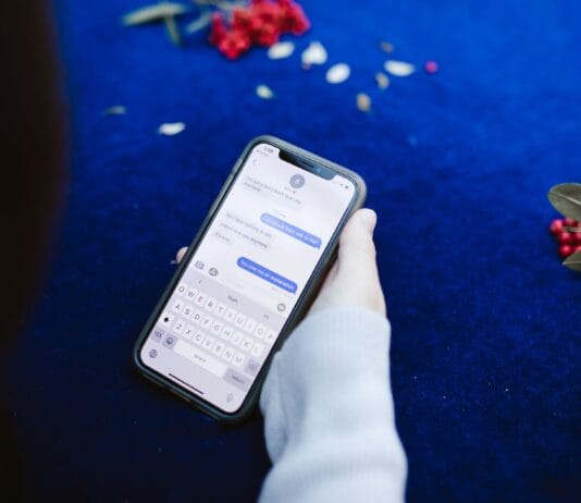 Osoba trzymająca smartfon z wiadomościami tekstowymi na niebieskim tle z kwiatam
